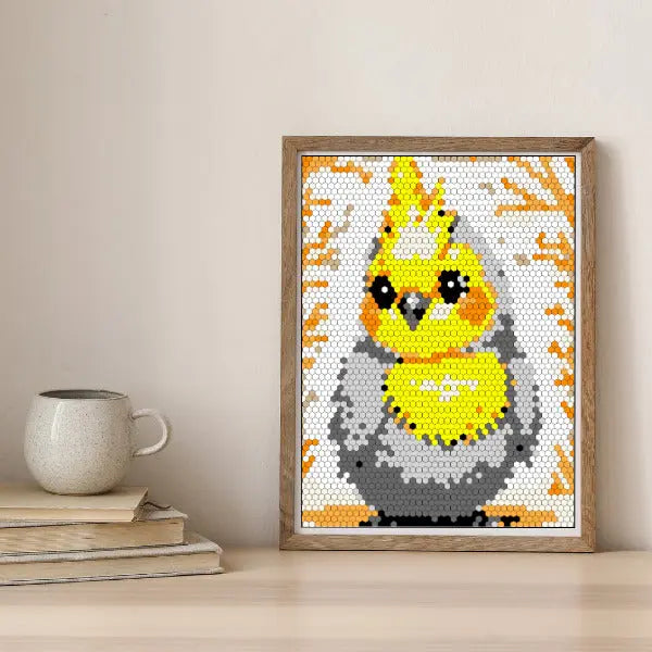 A framed color by number artwork depicting a yellow and gray cockatiel bird, created with a hexagonal mosaic pattern. The artwork is displayed on a light-colored wooden surface.