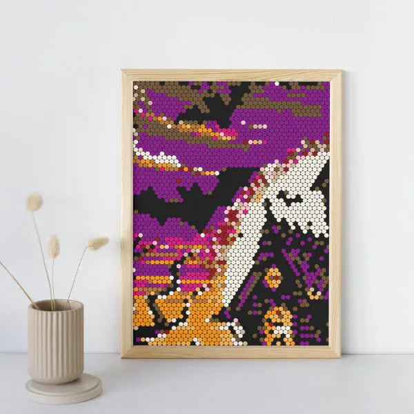 Framed Halloween color by number design showing a spooky haunted house with a pointed roof, a crescent moon, and bats flying in a purple and orange sky, displayed on a white wall next to a dried plant in a ribbed vase.